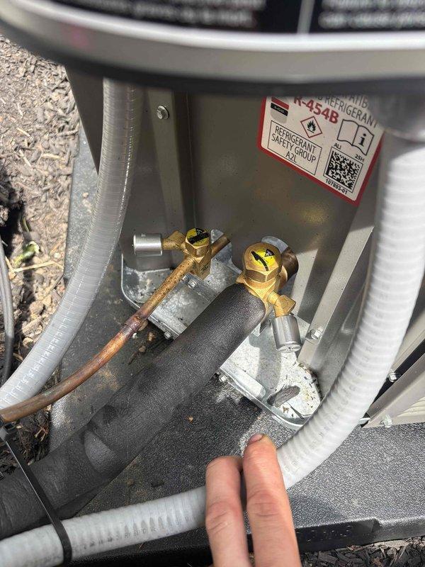 Conducted warranty inspection on recently installed outdoor condensing unit and identified missing tamper-proof caps on refrigerant service valves. Documented deficiency with photographs showing yellow standard caps instead of required tamper-proof caps on both liquid and suction line service ports. Job placed on hold pending manager approval for corrective action to meet code compliance requirements.