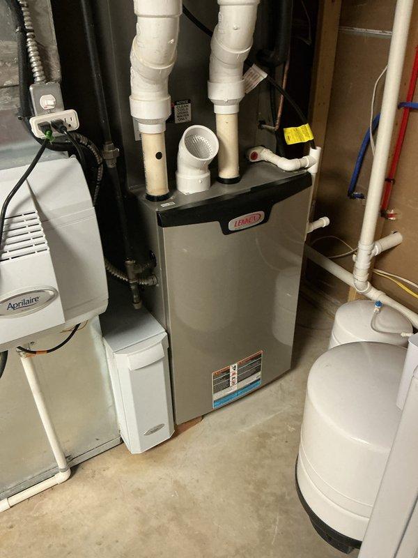 Completed MVP AC maintenance on Lennox HVAC system in basement utility room. Performed comprehensive cooling system inspection, including examination of furnace unit, electrical connections, and associated components. Inspected terminal block connections with multiple colored wires, noting dust accumulation and environmental exposure typical of basement installations. Verified proper operation of white PVC exhaust and intake vent pipes extending from furnace top. System operational and ready for cooling season.