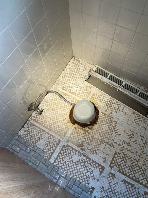 Responded to service call for two back-to-back upstairs bathrooms in 1970s-era home where toilets were improperly connected with a T fitting inside the wall, causing cross-flushing issues between fixtures. Upon arrival, homeowner had already removed existing toilet and tile flooring in preparation for plumbing modifications. Accessed concealed drain line connection within wall cavity and removed improper T fitting configuration. Installed code-compliant Y fitting to provide proper venting and drainage for both toilet fixtures, eliminating the cross-flow problem. Documented existing conditions showing prepared work area with exposed mosaic tile flooring and wall-mounted fixtures. Job placed on hold pending completion of restoration work; will return for final installation and testing when homeowner confirms area is ready for fixture reinstallation.