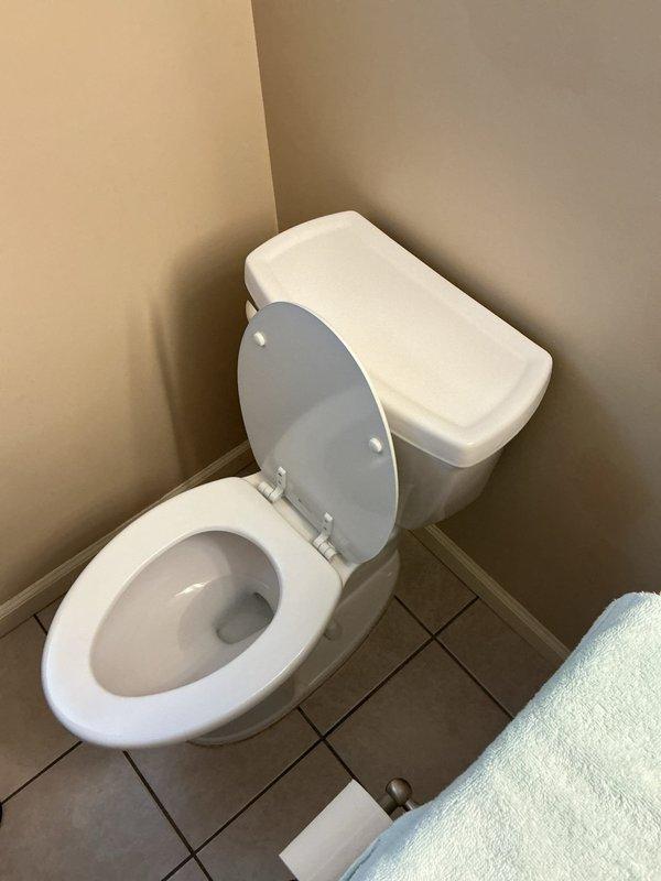 Responded to service call for two back-to-back upstairs bathrooms in 1970s-era home where toilets were improperly connected with a T fitting inside the wall, causing cross-flushing issues between fixtures. Upon arrival, homeowner had already removed existing toilet and tile flooring in preparation for plumbing modifications. Accessed concealed drain line connection within wall cavity and removed improper T fitting configuration. Installed code-compliant Y fitting to provide proper venting and drainage for both toilet fixtures, eliminating the cross-flow problem. Documented existing conditions showing prepared work area with exposed mosaic tile flooring and wall-mounted fixtures. Job placed on hold pending completion of restoration work; will return for final installation and testing when homeowner confirms area is ready for fixture reinstallation.