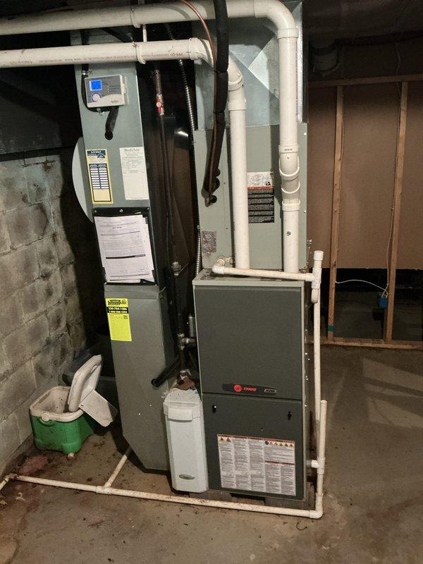 Completed full HVAC system installation including 90% efficiency Trane furnace and matching air conditioning condenser unit. Installed new furnace in basement mechanical room with proper venting using white PVC piping, connected refrigerant lines, and integrated digital control panel. Positioned outdoor AC condenser unit on existing pad adjacent to building structure, established electrical connections via wall-mounted panel, and verified proper gas line connections. All equipment tested and confirmed operational upon completion.