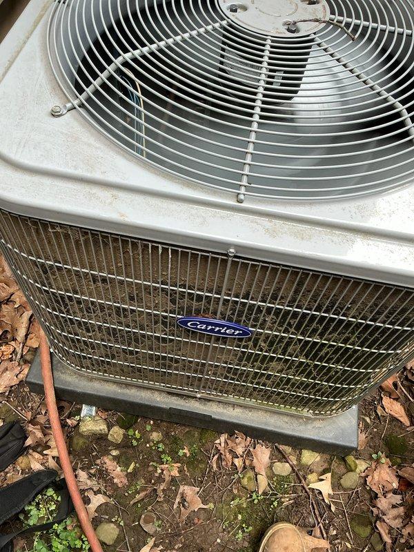 Performed comprehensive AC tune-up service on Carrier outdoor condensing unit located in wooded area with heavy leaf and debris accumulation. Cleaned condenser coil, fan assembly, and exterior housing which showed weathering and algae growth on front grille. Inspected indoor evaporator coil and air filter assembly, noting dust accumulation on mesh filter pad within air handler unit. Cleared leaves, rocks, and organic debris from around unit base and concrete pad to ensure proper airflow and drainage. System operational with no reported issues; routine maintenance completed to maintain efficiency and prevent future problems.