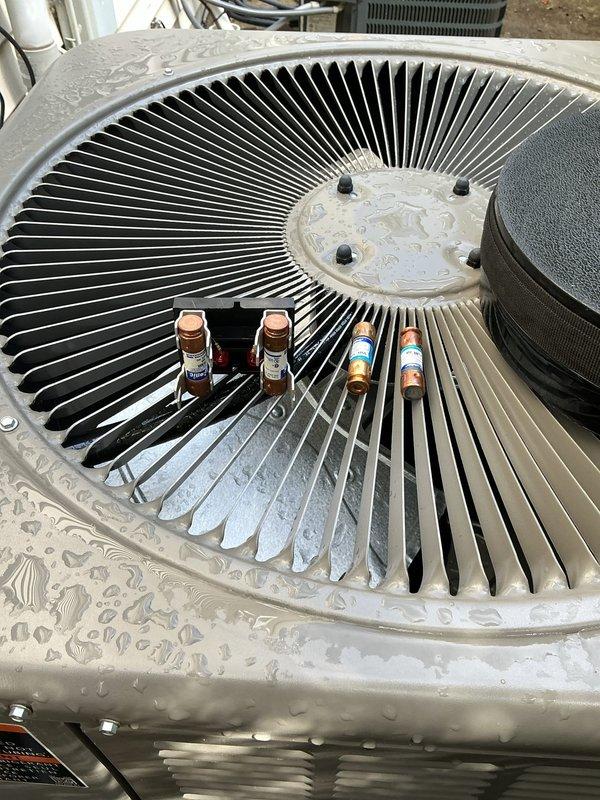 Responded to service call for non-operational air conditioning system on one-year-old Lennox condenser unit. Upon arrival, performed diagnostic inspection of outdoor unit including visual assessment of electrical components and fuse array. Inspected dual-fuse configuration with copper and color-coded caps, verified electrical connections, and assessed overall system condition. Unit found to be in operational status following inspection, with all major components including fan assembly and electrical panel functioning properly.