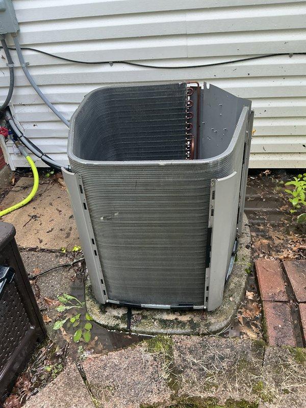 Performed comprehensive preventive maintenance on a 6-year-old residential air conditioning system located on ground-level concrete pad. Removed top panel and inspected all internal components including compressor, condenser coil, refrigerant lines, and electrical connections. Noted moderate dust and dirt accumulation on condenser coil fins requiring cleaning. Verified compressor mounting and isolation grommets were secure and properly positioned. Inspected copper refrigerant lines and connections for signs of wear or leakage. Checked electrical conduit routing and cable connections along exterior wall. Cleared debris, fallen leaves, and organic material from around unit base and concrete pad to ensure proper airflow and drainage. System operational and functioning within normal parameters upon completion of maintenance service.