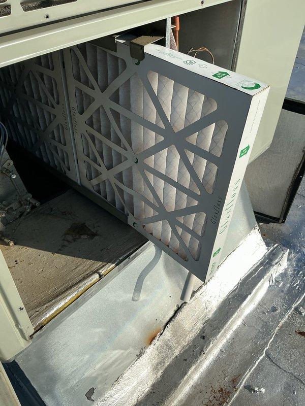 Completed BS-MVP cooling maintenance visit on rooftop unit requiring ladder access. Inspected air handling system and replaced air filter with clean pleated media filter. Observed significant corrosion and oxidation on copper refrigerant coil assembly, indicating potential moisture exposure and age-related deterioration. Documented equipment condition with photos showing corroded copper tubing with reddish-orange patina and interior cabinet components. System operational at time of service completion.