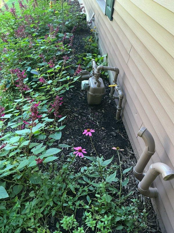 Installed natural gas line from residential structure to exterior fire pit. Ran gray flexible gas conduit along building foundation, securing to exterior wall with appropriate mounting hardware. Extended gas line approximately 30-40 feet from house connection point to fire pit location. Terminated line at circular paver stone fire pit with proper fittings for fire feature connection. Verified all connections for proper seal and conducted pressure test to ensure system integrity and safety compliance.
