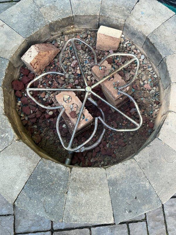 Installed natural gas line from residential structure to exterior fire pit. Ran gray flexible gas conduit along building foundation, securing to exterior wall with appropriate mounting hardware. Extended gas line approximately 30-40 feet from house connection point to fire pit location. Terminated line at circular paver stone fire pit with proper fittings for fire feature connection. Verified all connections for proper seal and conducted pressure test to ensure system integrity and safety compliance.