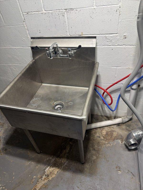 # Plumbing Service Completed

Responded to a comprehensive plumbing service call addressing multiple system issues throughout the property. Primary focus involved snaking the downspout drain to clear blockages and restore proper drainage flow. Removed a malfunctioning garbage disposal unit from the kitchen sink assembly. 

Inspected the tankless water heater and identified significant mineral buildup requiring descaling service to restore efficiency and proper operation. Noted the absence of a drain line installation for the temperature and pressure relief valve, which presents a code compliance concern.

Addressed basement plumbing needs by removing the existing toilet fixture and properly capping the drain line to prevent sewer gas infiltration and prepare the area for future use. 

Identified a leak in the cast iron stack line requiring repair to prevent water damage and maintain the integrity of the main drainage system. Documentation photos captured the utility area ceiling showin