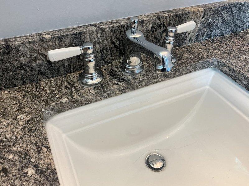Replaced Kohler cartridge on right-side fixture assembly, addressing both hot and cold water control issues on three-piece deck-mounted faucet with white porcelain lever handles. Accessed supply lines through vanity cabinet, installed new cartridge components, and verified proper operation of both temperature control valves. All plumbing connections tested and confirmed leak-free upon completion.