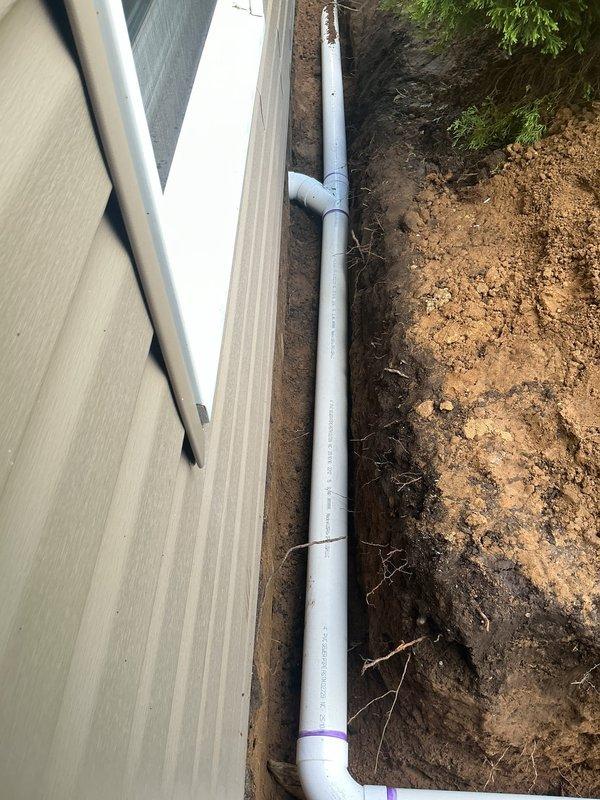 Installed new 4" downspout drainage system for front of residence, connecting garage drains, front door downspout, and corner garage downspout. Trenched new drainage lines from building foundation to front ditch, tunneling under sidewalk where necessary. Daylighted discharge pipe at ditch terminus with gravel surround for erosion control. All white PVC piping installed with proper slope and secure connections to existing downspout system to direct water away from foundation.