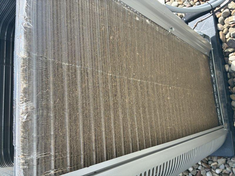Completed preventive maintenance service on a one-year-old ground-mounted air conditioning condenser unit. Inspected heat exchanger coils and noted significant accumulation of dust, dirt, pollen, and outdoor debris throughout the aluminum fins, with visible discoloration and drainage patterns indicating environmental exposure. Performed thorough cleaning of condenser coils to restore proper airflow and heat transfer efficiency, checked refrigerant lines for proper insulation, verified unit operation, and confirmed system is ready for continued cooling season performance.