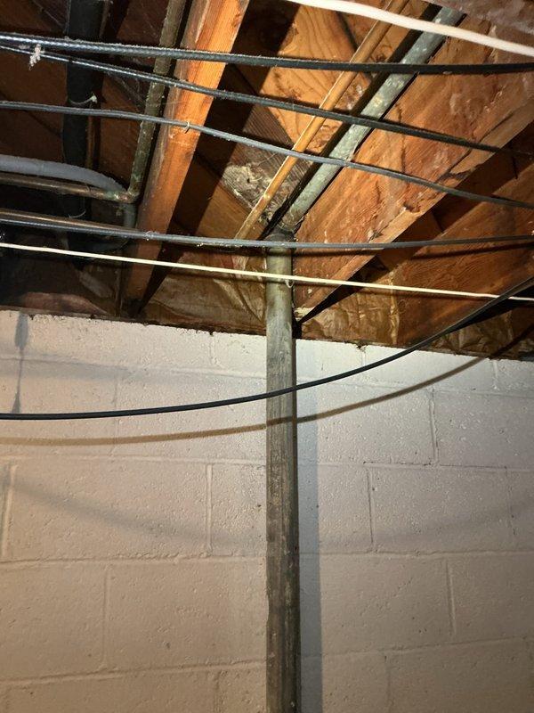 Responded to a plumbing service call for a leaking first-floor tub drain caused by severe corrosion on the drain pipe assembly. Upon inspection in the basement area below the fixture, discovered extensively corroded pipe fittings and valve assemblies with heavy rust and oxidation buildup compromising the integrity of the drain system. Documented the deteriorated plumbing infrastructure showing the corroded connections and aged piping requiring replacement to resolve the active leak condition.