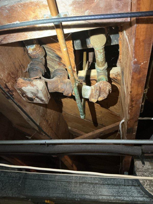 Responded to a plumbing service call for a leaking first-floor tub drain caused by severe corrosion on the drain pipe assembly. Upon inspection in the basement area below the fixture, discovered extensively corroded pipe fittings and valve assemblies with heavy rust and oxidation buildup compromising the integrity of the drain system. Documented the deteriorated plumbing infrastructure showing the corroded connections and aged piping requiring replacement to resolve the active leak condition.