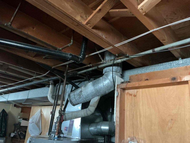 Responded to service call for reported furnace stack leak on 18-year-old heating system. Upon arrival, performed comprehensive visual inspection of furnace flue pipe assembly running from basement through attic to roof penetration. Examined all accessible sections of vent stack, including connections, joints, and support points throughout the vertical run. Inspected attic area where metallic ductwork and copper piping intersect with wooden structural members, checking for signs of moisture intrusion, condensation staining, or water damage on surrounding materials. Evaluated basement installation, including PVC drainage system and proximity to furnace exhaust components. Photographed critical areas showing vent configuration, pipe routing through floor joists, and overall system condition for documentation purposes. No active leaks observed during inspection period, though recommended monitoring during heating cycle operation to identify potential condensation issues that may occur unde