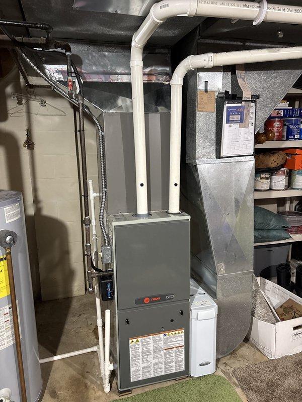 Completed installation of new air conditioning system including outdoor condensing unit and indoor evaporator coil. Outdoor unit was positioned on concrete pad against exterior brick wall with proper clearances maintained, electrical disconnect box mounted to structure, and line set connected between indoor and outdoor components. Indoor evaporator coil was installed in conjunction with existing Trane furnace in basement utility area, with refrigerant lines and condensate drainage properly routed through PVC piping. System was pressure tested for leaks, evacuated to manufacturer specifications, charged with appropriate refrigerant, and cycled through operational testing to verify proper cooling performance and airflow.