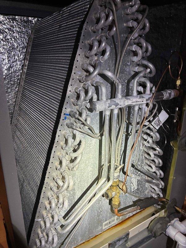 Completed biennial preventive maintenance inspection on residential air conditioning system. Thoroughly cleaned outdoor condenser coil which exhibited moderate to heavy accumulation of dirt, dust, and organic debris throughout the fin surfaces. Inspected indoor evaporator coil assembly in attic installation, noting normal operational condensation and light dust accumulation on serpentine coil pattern. Verified refrigerant line connections, brass fittings, and insulation integrity on both suction and liquid lines. Checked electrical connections and control wiring. System operating within normal parameters following maintenance service.