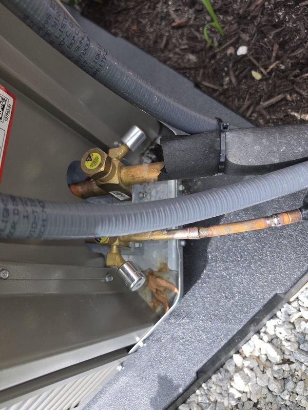 Conducted warranty inspection on recently installed HVAC system and identified multiple deficiencies requiring correction. Found only one locking cap properly installed on compressor service port, with second cap improperly placed on equipment platform instead of refrigerant line connection. Documented that installing contractor failed to provide required smoke/carbon monoxide detectors to occupant as part of installation scope. Photographed improperly secured service port caps on outdoor condensing unit showing exposed refrigerant line connections, corroded copper piping with visible oxidation, and weathered insulation. Also documented smoke detector that should have been provided during initial installation. Placed job on hold pending management review and approval for corrective action by original installing contractor to address safety and code compliance issues.