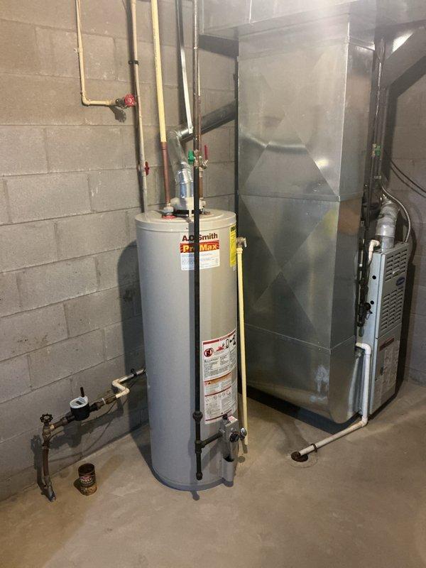 # HVAC Install - Complete System

Completed full residential HVAC system installation in basement mechanical room, including 90% AFUE furnace, 2410 CFM air conditioning system rated at 600 capacity, integrated air scrubber for indoor air quality enhancement, and new hot water heater. Installed white residential furnace unit with proper venting configuration using silver metal elbow connector and black flexible ductwork routed through ceiling. Connected furnace to rectangular metal supply plenum with silvery-gray finish for optimal air distribution throughout home.

Installed cylindrical water heater with Smith branding, featuring yellow manufacturer label on upper portion and complete safety specification labeling on tank front. Configured all copper and metal piping connections with red valve handles for water supply control. Installed pressure relief valve with blue and white components on upper piping assembly per code requirements. All plumbing connections properly secured and test