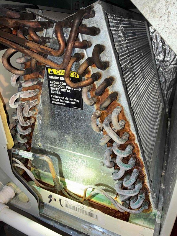 Completed preventive maintenance cooling visit on 10-year-old air conditioning system. Inspected outdoor condensing unit and indoor evaporator coil assembly, documenting existing capacitor with visible weathering and corrosion on terminal connections, as well as significant oxidation and rust buildup on evaporator coil copper tubing. Unit operational at time of inspection with all electrical connections secure and system functioning within normal parameters for equipment age.
