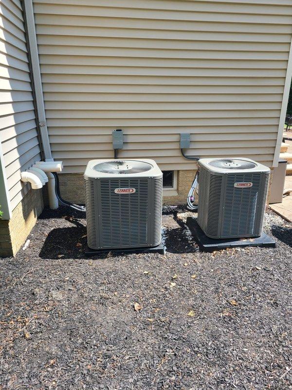 Completed installation of dual Lennox air conditioning condensing units with new coils as first AC system for the property. Replaced failed FLNR 40 amp fuses during installation, mounted both outdoor units on vibration-isolating pads with proper clearances, and connected refrigerant lines and electrical service including conduit runs along exterior wall.