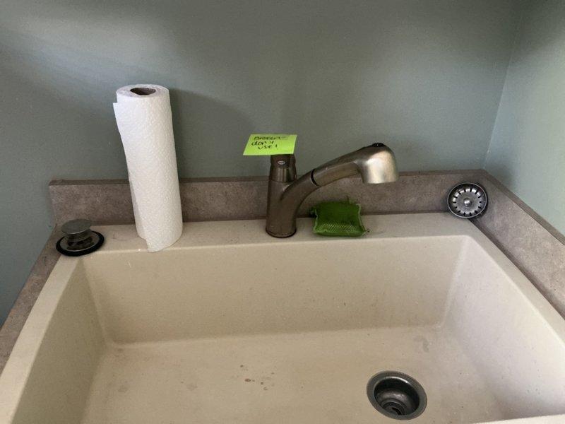 Responded to a water leak under the laundry room sink and discovered significant water damage to the particle board cabinet floor, with visible staining, discoloration, and mineral deposits indicating prolonged moisture exposure. Inspected the plumbing connections, including the disposal assembly, flexible supply lines, and shut-off valves to identify the source of the leak. Documented the extent of the water damage to the cabinet base for repair recommendations.