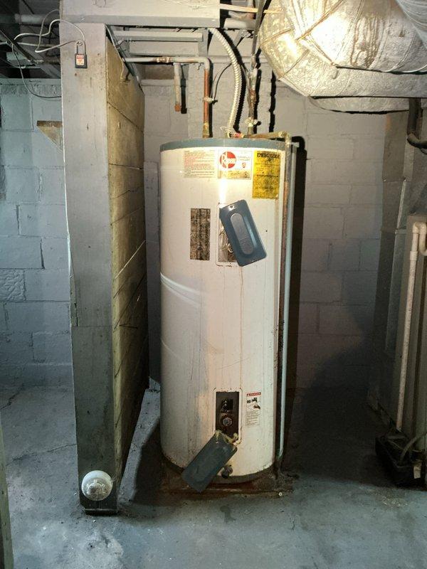 Conducted on-site assessment of existing residential water heater installation in basement utility area. Documented current unit condition, noting significant age-related deterioration including rust staining at tank base and general wear on exterior surfaces. Evaluated existing plumbing connections, including copper supply lines, brass shutoff valves, and pressure regulation equipment. Photographed water heater specifications, electrical connections, and mechanical infrastructure to determine replacement requirements. Assessed utility room layout, clearances, and access points for future water heater replacement installation.