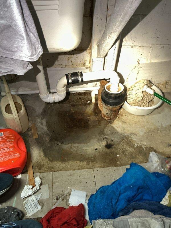 Responded to slow-draining basement floor drain service call. Upon inspection, discovered severely corroded cast iron drain pipe with significant rust buildup and scale accumulation restricting water flow. The deteriorated pipe interior showed extensive oxidation throughout, with compromised structural integrity evident at connection points to PVC drainage system. Documented existing conditions including standing water on basement floor, corroded metal fixtures, and aging plumbing infrastructure requiring attention. Assessed drainage system configuration and identified the corroded pipe section as primary cause of slow drainage issue.