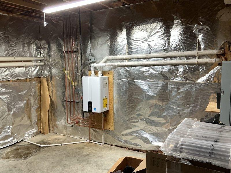 Successfully installed Navien NPE 240A2 tankless water heater in basement, wall-mounted on wooden backing board. Reused existing exhaust and intake penetrations from previous tankless boiler installation, routed condensate drain to floor drain, and connected to existing gas line and water supply lines with copper piping. Electrical connection completed using nearby outlet, and all plumbing connections secured with appropriate mounting brackets and shut-off valves.