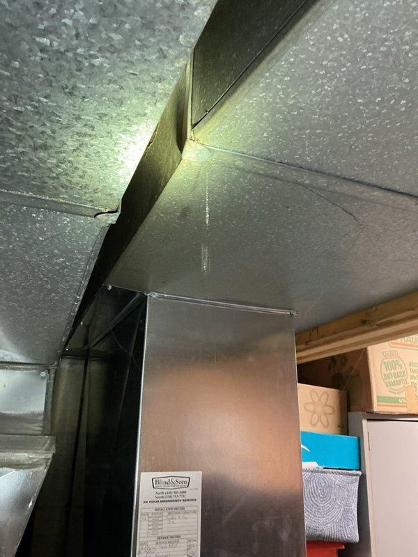 Responded to service call for water dripping from air duct near furnace. Upon inspection, discovered extensive condensation accumulation on metallic ductwork surfaces throughout the area, with visible water droplets covering the exterior of the ducts. Identified a separation point in the ductwork where sections had pulled apart, creating a gap that was allowing conditioned air to escape and contributing to moisture issues. The heavy condensation indicated significant temperature differential between the duct interior and ambient conditions in the utility space. Documented conditions with photographs showing the extent of moisture accumulation and structural separation in the ductwork system requiring repair to prevent continued water damage.