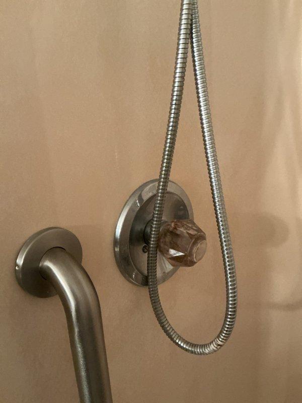 Responded to service call for dripping shower fixture. Upon arrival, inspected handheld showerhead assembly and identified mineral buildup and corrosion at the hose-to-wall mount connection point, which was causing the leak. Removed existing showerhead, cleaned connection threads, and installed new showerhead assembly with fresh plumber's tape to ensure proper seal. Tested water flow and verified leak was eliminated. Accessed plumbing through existing wall panel to confirm no additional issues with supply lines.