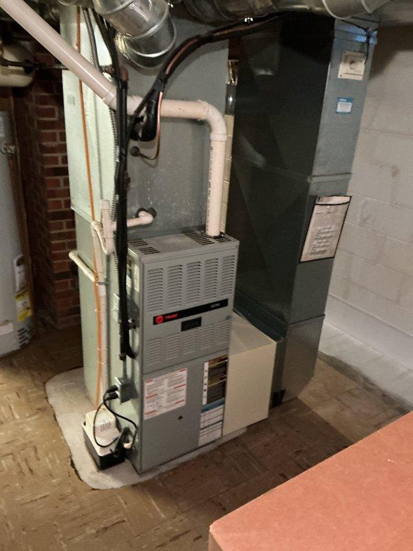 # HVAC Install - Complete System

## Summary
Completed full HVAC system installation including 90% efficiency furnace with humidifier and matching air conditioning unit, verified proper venting installation to ensure flues are not cellular core construction.

## Work Performed

Installed complete residential heating and cooling system in basement mechanical room and exterior location. System consists of Trane brand furnace unit with integrated humidifier and corresponding outdoor condensing unit.

**Indoor Equipment Installation:**
- Mounted gray metal furnace unit on concrete basement floor
- Connected white PVC intake and exhaust venting from furnace, routing upward through structure
- Verified all flue pipes are appropriate non-cellular core material per code requirements
- Installed electrical connections with proper wiring run along installation perimeter
- Connected silver metallic supply ductwork to furnace plenum
- Positioned tall air handler unit adjacent to furnace with prope