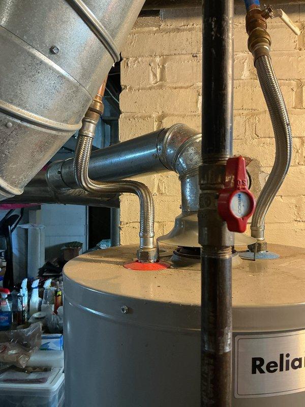 Completed new water heater installation in basement utility area of residential property. Removed existing unit and installed Reliance brand residential water heater with proper venting configuration. Connected cold water supply and hot water outlet lines using flexible braided stainless steel connectors with brass fittings. Installed red-handled ball valve on supply line for system isolation. Integrated installation with existing PEX distribution system including red hot water and blue cold water lines secured to ceiling joists. Verified all connections for proper seal and tested system operation. Confirmed temperature and pressure relief valve installation and proper discharge piping. Unit positioned on concrete floor against cinderblock wall with adequate clearance for service access and code compliance.