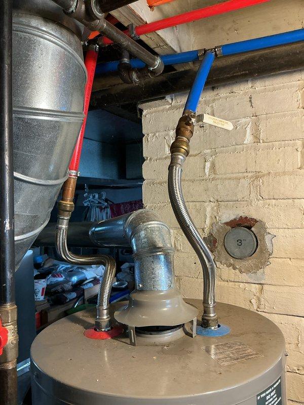 Completed new water heater installation in basement utility area of residential property. Removed existing unit and installed Reliance brand residential water heater with proper venting configuration. Connected cold water supply and hot water outlet lines using flexible braided stainless steel connectors with brass fittings. Installed red-handled ball valve on supply line for system isolation. Integrated installation with existing PEX distribution system including red hot water and blue cold water lines secured to ceiling joists. Verified all connections for proper seal and tested system operation. Confirmed temperature and pressure relief valve installation and proper discharge piping. Unit positioned on concrete floor against cinderblock wall with adequate clearance for service access and code compliance.