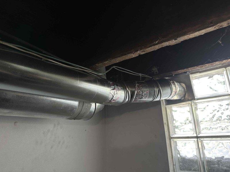 Installed new dryer vent system in basement laundry area, routing ductwork vertically then horizontally to exit through the right side of the space. Due to recent waterproofing concerns, the exhaust was routed to avoid penetrating exterior walls near the glass block window. Metallic ductwork was secured with proper seaming and aluminum tape at all joints, ensuring code-compliant ventilation for the dryer appliance.