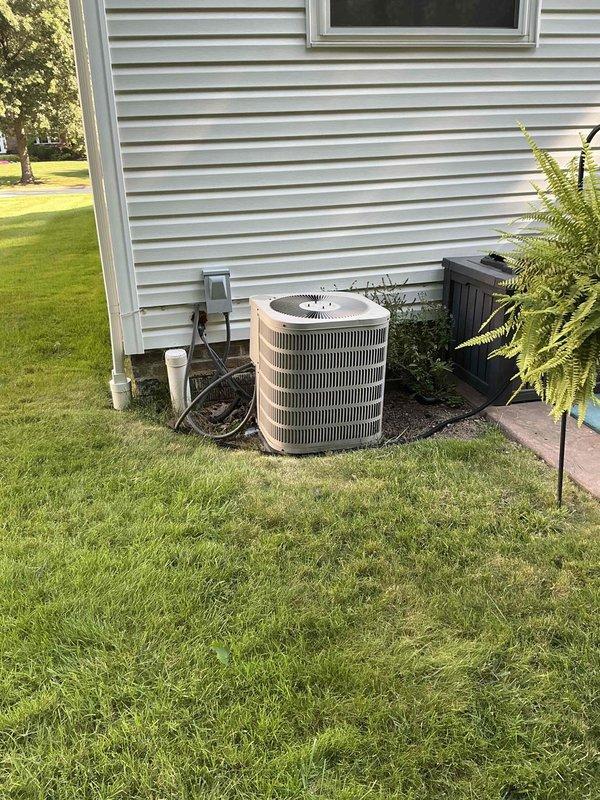 Performed on-site evaluation of 25-year-old residential air conditioning system for replacement estimate. Inspected exterior cylindrical condenser unit with beige housing and vertical louvers, noting age and condition of equipment mounted on concrete pad adjacent to home's exterior. Documented basement furnace and HVAC infrastructure, including ductwork, electrical connections, and existing system components to assess compatibility requirements for new AC installation. Captured photographic documentation of current equipment configuration and installation location for replacement planning purposes.