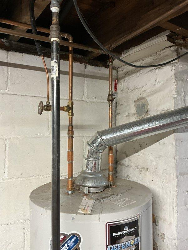 Conducted on-site evaluation of existing Bradford White Defender water heater system in basement utility area. Inspected 15.5-year-old conventional tank water heater showing visible signs of age including surface wear and exterior discoloration. Assessed all plumbing connections including copper supply lines, brass shut-off valves, and vent piping configuration. Examined condition of piping system noting natural oxidation and patina on copper components consistent with age of installation. Evaluated mechanical room layout and existing infrastructure to determine feasibility for both conventional tank replacement and tankless water heater conversion options. Documented current installation configuration including all connections, venting arrangements, and available utility access points. Photographed equipment and surrounding plumbing infrastructure to support estimate preparation. Prepared comprehensive pricing proposal covering both standard tank water heater replacement and alternati
