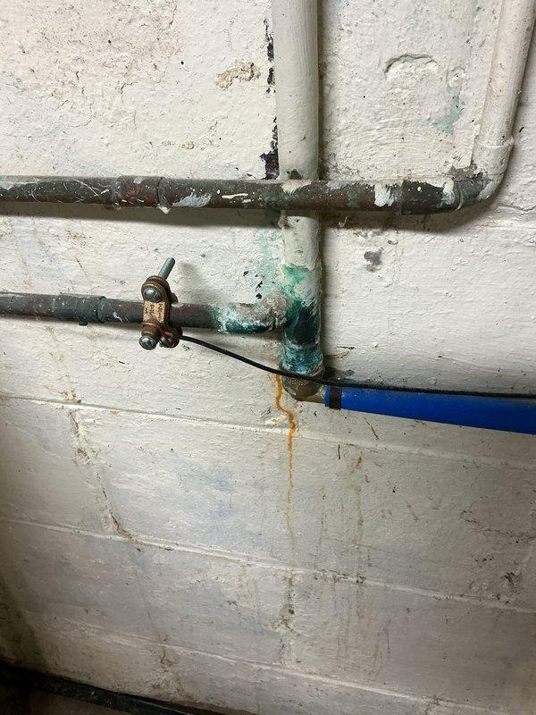 Inspected and assessed corroded washer hookup valves and associated plumbing prior to new appliance installation. Found frozen shut-off valve with significant corrosion and green patina on brass components, causing minor drip when operated. Documented extensive deterioration on metal piping including surface rust and oxidation on horizontal supply lines. Identified mixed-age plumbing system with newer PVC and blue plastic piping connected to older corroded metal components. Photographed valve assemblies, pipe conditions, and wall-mounted fixtures showing rust staining and water damage on surrounding surfaces for customer review and repair recommendations.