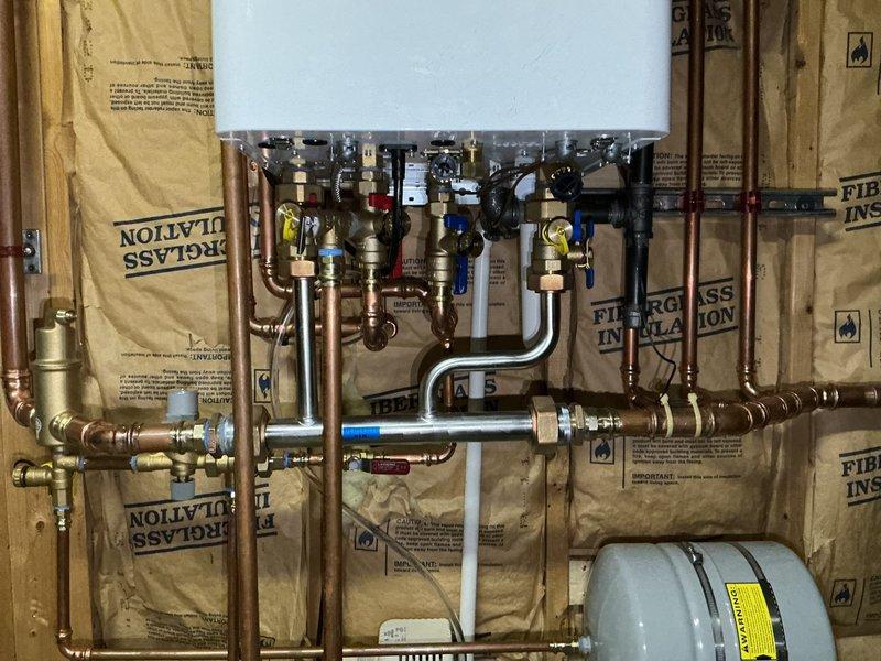 Successfully completed installation of combination boiler system with four-zone hydronic heating distribution. Installed comprehensive copper piping network with multiple blue-handled ball valves for zone isolation, black distribution manifolds with brass fittings, and gray expansion tank for system pressure management. Mounted all components to interior wall studs during rough-in phase, incorporating stainless steel flexible connectors and proper valve placement throughout. Staged and integrated condensate pump with tubing, complete boiler kit, and all necessary mounting hardware. Installed REHAU PEX piping runs across ceiling joists with proper hangers and brackets, connecting to existing infrastructure. All zones properly manifolded and valved for independent temperature control, with system ready for insulation and finish work.