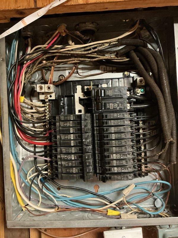 Replaced existing garage sub panel with new electrical panel box mounted in wooden cabinet enclosure. Installed new 20-amp dedicated GFCI-protected circuit with proper wire routing and connections. Organized multiple branch circuits including red, blue, yellow, and gray conductors entering panel, ensuring all breakers were properly seated on bus bars and all connections were secure. Verified proper grounding configuration and confirmed all circuits operational upon completion.