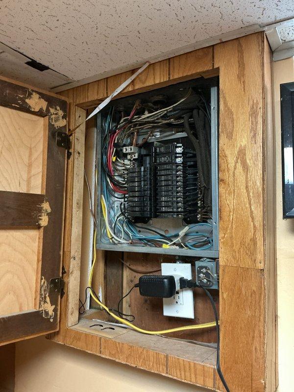 Replaced existing garage sub panel with new electrical panel box mounted in wooden cabinet enclosure. Installed new 20-amp dedicated GFCI-protected circuit with proper wire routing and connections. Organized multiple branch circuits including red, blue, yellow, and gray conductors entering panel, ensuring all breakers were properly seated on bus bars and all connections were secure. Verified proper grounding configuration and confirmed all circuits operational upon completion.