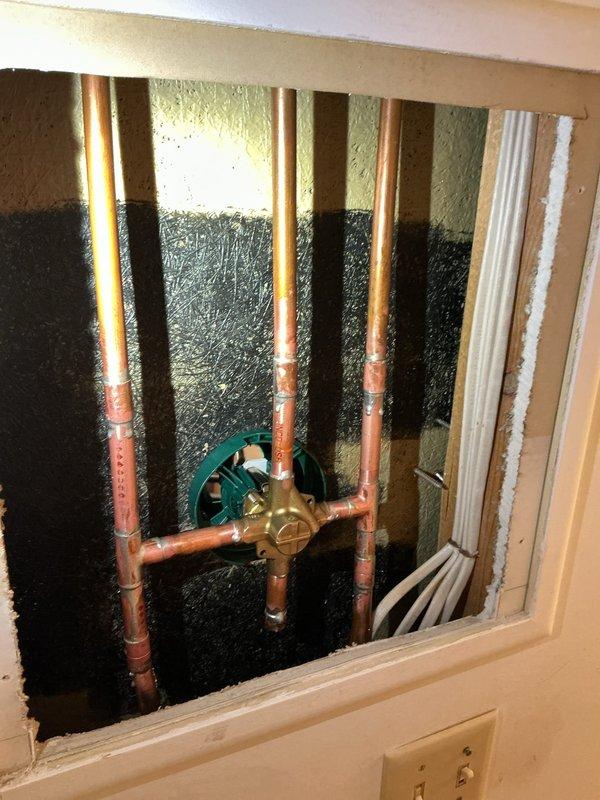 Replaced a dripping Delta shower faucet with a new Moen Chateau shower faucet assembly. Accessed the plumbing through an existing access panel, which required enlargement at the bottom for proper clearance. Installed new shut-off valves along with necessary copper pipe and brass fittings to complete the installation. All connections were secured and tested for proper operation and leak-free performance.