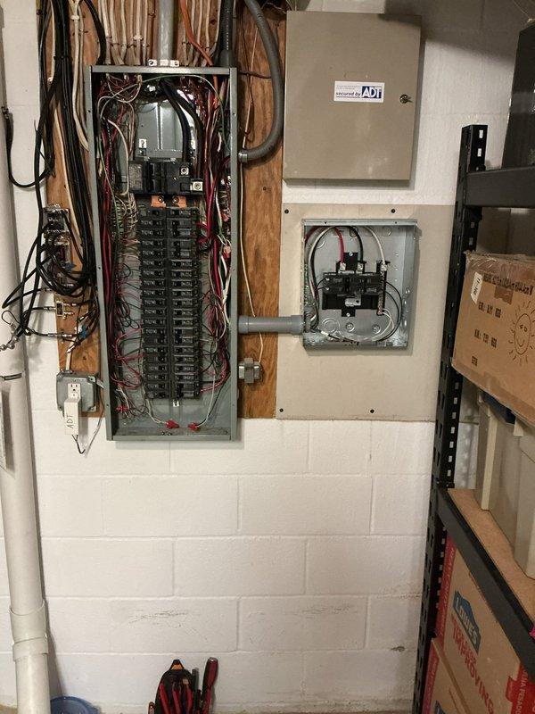 Installed a new sub panel adjacent to the main electrical panel in the basement and redistributed existing circuits to accommodate two 60-amp feed breakers in the main panel. Ran PVC conduit across exterior brick wall from service entrance to garage, entering low and routing up to a surface-mounted sub panel installed to the right of the refrigerator. From the garage panel, installed dedicated conduit run to the right wall, establishing three separate circuits: two 20-amp 120V standard receptacles and one 20-amp 240V receptacle with 5-20P configuration on the far right.