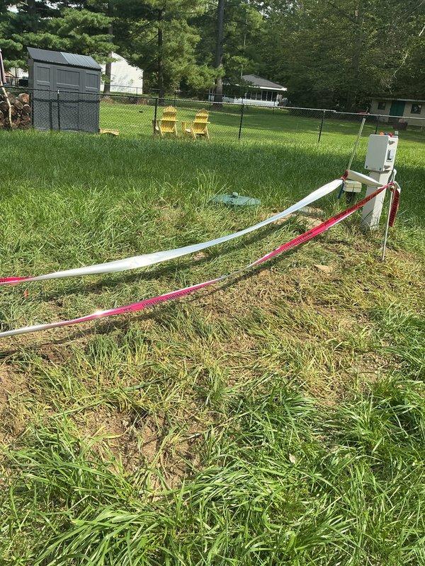 Completed post-inspection trench backfilling for underground electrical conduit installation. Filled and graded excavated trench where red and white PVC conduits run from pole-mounted meter base across lawn area, restoring ground surface to grade level. Work performed without requiring customer presence on site.