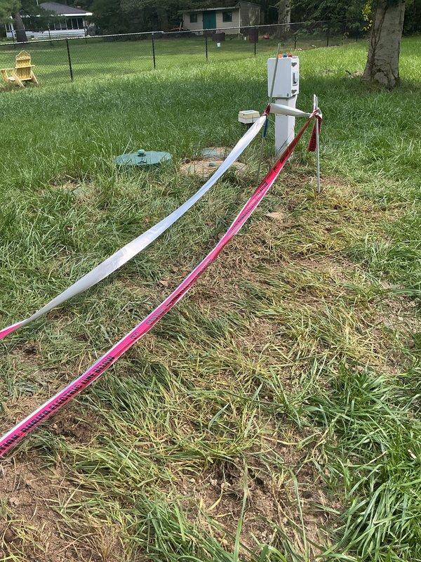 Completed post-inspection trench backfilling for underground electrical conduit installation. Filled and graded excavated trench where red and white PVC conduits run from pole-mounted meter base across lawn area, restoring ground surface to grade level. Work performed without requiring customer presence on site.