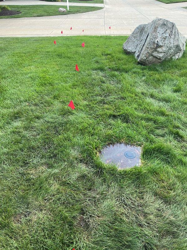 Responded to natural gas leak call near meter vault. Upon arrival, located circular brick-paved meter vault access point in front lawn area. Conducted thorough leak detection survey using appropriate gas detection equipment. Marked underground utility lines with red safety flags to establish work zone and ensure safe excavation parameters. Identified leak source at service connection point adjacent to meter vault assembly. Verified leak location and documented conditions with photographic evidence showing meter vault installation and marked utility corridor. Completed initial assessment and prepared site for repair procedures while maintaining safety protocols for natural gas service work.