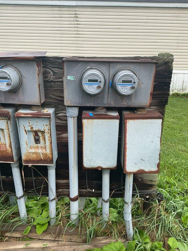 Performed comprehensive inspection of exterior electrical meter base and service equipment to facilitate utility power restoration. Documented extensive corrosion and weathering on meter panel enclosure, internal bus bars, and terminal connections. Assessed condition of service entrance conductors, mounting hardware, and multiple meter installations showing significant age-related deterioration requiring attention for code compliance and safe operation.