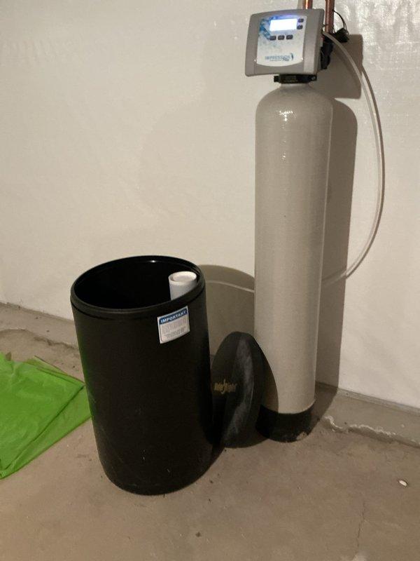 Completed salt delivery and replenishment service for residential water softening system. Upon arrival, accessed basement utility area where dual-tank water treatment system is installed. Inspected existing water softener configuration consisting of primary tan-colored resin tank with digital control head and secondary black brine tank. 

Removed brine tank lid and assessed current salt level, which had depleted to approximately 50% capacity. Delivered and loaded water softener salt into the black brine tank, replenishing supply to optimal operating level. Verified proper distribution of salt pellets within tank and confirmed white standpipe positioning remained secure and unobstructed for proper brine draw function.

Conducted visual inspection of system components including digital control head display readings, copper supply piping, and flexible tubing connections. All equipment appeared to be functioning within normal parameters with no visible leaks or mechanical issues noted. Sys