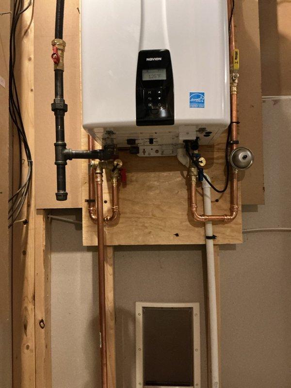 Removed existing 40-gallon power vent water heater and installed new Navien NPE-240A2 tankless water heater. Unit was wall-mounted on plywood backing near original tank location with all necessary supply and return piping reconfigured using copper pipe and PEX connections. Gas line was replumbed to accommodate new unit specifications, condensate drain line was routed to floor drain, and exhaust/intake air lines were installed with termination on south exterior wall near gas meter. Installation includes 12-year heat exchanger warranty, 5-year parts warranty, and 1-year labor warranty.