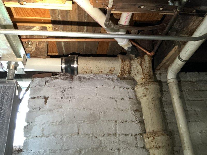 Responded to a main line repair call where a hole was discovered in the drain pipe connecting the toilet to the main plumbing stack. Upon inspection of the basement area, identified the damaged section of pipe along with extensive rust staining and water damage on the foundation walls and floor joists, indicating long-term moisture infiltration from the compromised pipe. The affected area showed significant deterioration with visible staining concentrated around the pipe penetrations and corner sections.

Performed diagnostic evaluation of the drainage system, documenting the condition of both the damaged pipe and the aging cast iron plumbing stack. Photographed the existing plumbing infrastructure, including white PVC drain lines, copper supply lines, and the deteriorated iron stack showing signs of corrosion and age-related wear. The inspection revealed multiple pipe connections and fittings in the basement ceiling area, with evidence of previous water damage and staining on wooden j