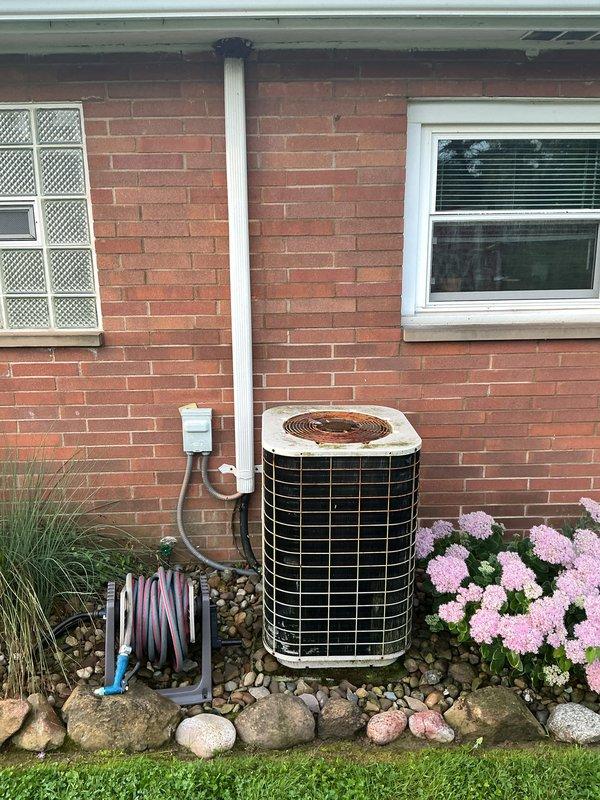 Completed full HVAC system installation including indoor Airtemp wall-mounted air handler and outdoor condensing unit. The indoor unit was installed in a recessed wall cavity with proper electrical connections, refrigerant line set, and condensate drainage. The outdoor condenser was positioned on a gravel pad against the exterior brick wall with appropriate clearances, connected to a wall-mounted electrical disconnect box, and linked to the indoor unit via copper refrigerant lines and PVC condensate piping. System was tested and verified operational.